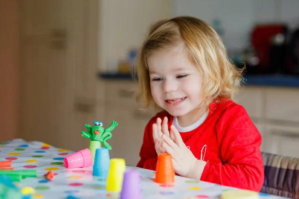 Очаровательная милая маленькая девочка с красочной глиной. Здоровый ребенок играет и создает игрушки из теста. Маленький ребенок моделирует когти и учится — стоковое фото