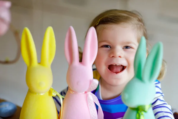 Niedlichen kleinen Mädchen mit drei farbigen Pastellhasen glückliches Baby Kind Spaß mit Osterdekorationen Hase in rosa, gelb und grün. entzückendes gesundes lächelndes Kind im Familienurlaub — Stockfoto