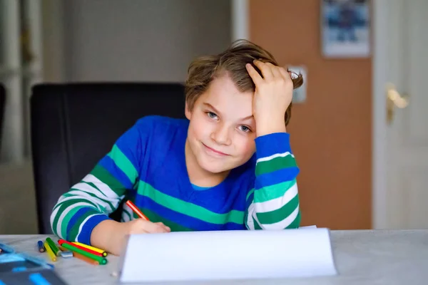 Portrait of cute happy school kid boy at home making homework. Little child writing with colorful pencils, indoors. Elementary school and education. Kid learning writing letters and numbers