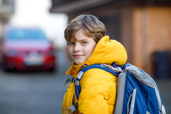 Malý kluk ze základní školy, co chodí do školy. Portrét šťastného dítěte na ulici s dopravou. Student ve žluté bundě a batoh v barevných zimních šatech. — Stock fotografie