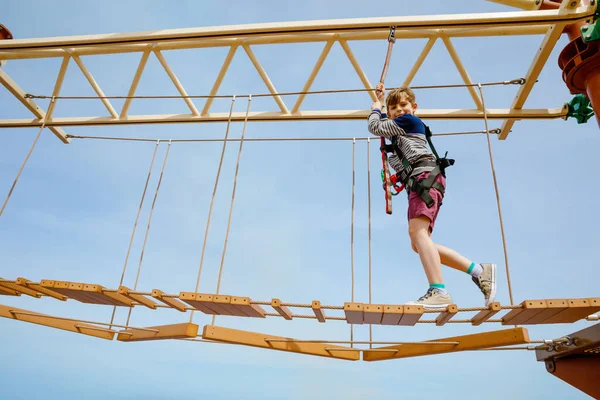 Feliz niño trepando por el sendero de la cuerda alta. Niño activo haciendo aventura y acción en vacaciones familiares. Desafío para niños valientes . — Foto de Stock