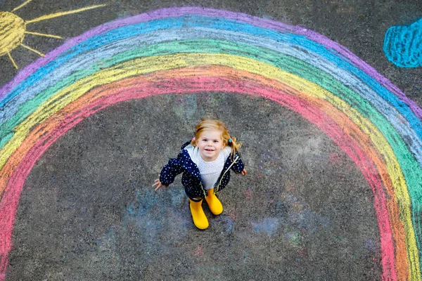 Happy Little småbarn flicka i gummistövlar med regnbåge sol och moln med regn målade med färgglada Chalks på marken eller asfalt på sommaren. Söta barn ha roligt. kreativ fritid — Stockfoto