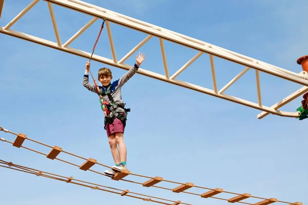 Feliz niño trepando por el sendero de la cuerda alta. Niño activo haciendo aventura y acción en vacaciones familiares. Desafío para niños valientes . —  Fotos de Stock