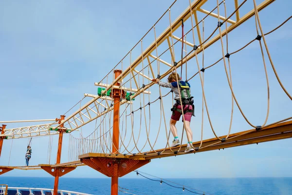 Feliz niño trepando por el sendero de la cuerda alta. Niño activo haciendo aventura y acción en vacaciones familiares. Desafío para niños valientes . — Foto de Stock