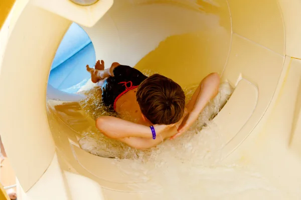 Piccolo ragazzo felice che scivola sul tubo dell'acquascivolo nel parco del resort. Bambino sano divertirsi . — Foto Stock