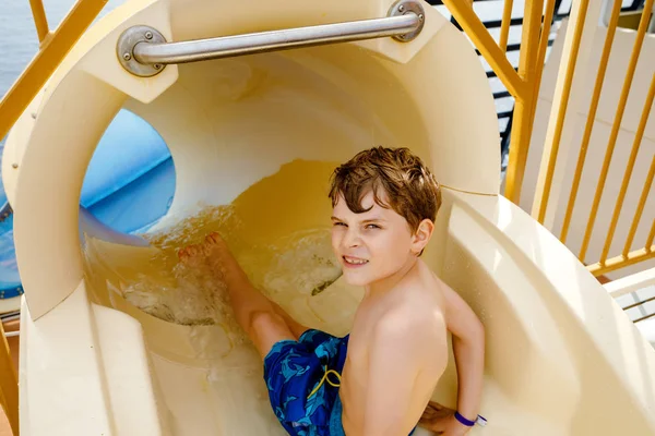 Piccolo ragazzo felice che scivola sul tubo dell'acquascivolo nel parco del resort. Bambino sano divertirsi . — Foto Stock