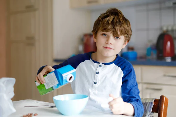 Glücklicher kleiner blonder Junge, der Müsli zum Frühstück oder Mittagessen isst. gesunde Ernährung für Kinder. Kind im bunten Pyjama frühstückt mit Milch und Müsli. — Stockfoto