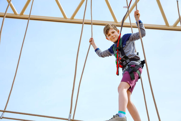 Happy little kid boy climbing on high rope course trail. Active child making adventure and action on family vacations. Challenge for brave kids.