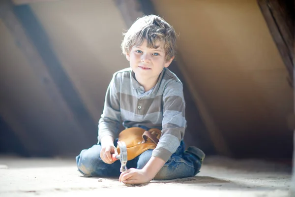 Kleiner Junge hilft mit Spielzeug auf Baustelle. Lustiges Kind von 6 Jahren, das Spaß am Bau eines neuen Familienhauses hat. Kind mit Nägeln und Hammer hilft Vater bei Renovierung von altem Haus. — Stockfoto