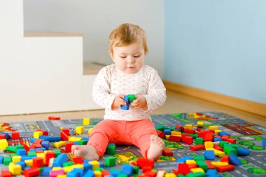 Eğitici oyuncaklarla oynayan sevimli bir kız bebek. Mutlu sağlıklı bir çocuk, evdeki renkli tahta bloklarla eğleniyor. Bebek öğrenme renkleri ve biçimleri