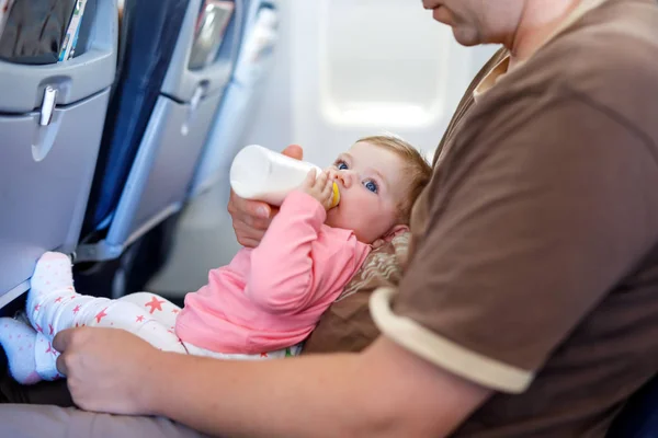 Батько тримає доньку під час польоту на літаку, їде у відпустку. Дитяча дівчинка п'є молоко з пляшки. Авіаперевезення з дитиною, дитиною та сімейною концепцією. Втомлений чоловік подорожує з дітьми . — стокове фото