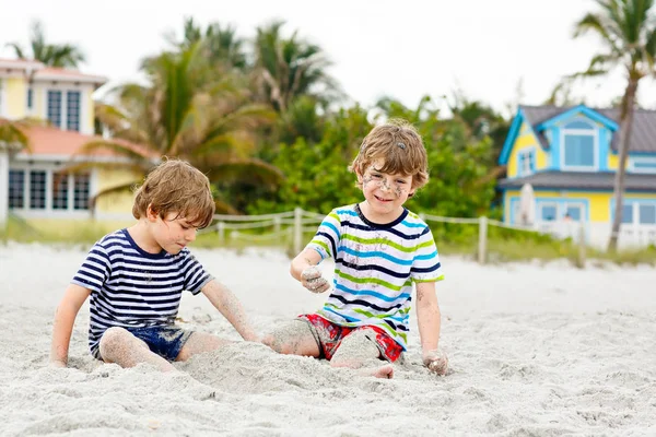 Двоє маленьких дітей бавляться на тропічному пляжі, з найкращими друзями, з концепцією дружби. Брати і сестри, близнюки в родині, виглядають з пальмами на задньому плані. Сімейні канікули в Неаполі (США). — стокове фото