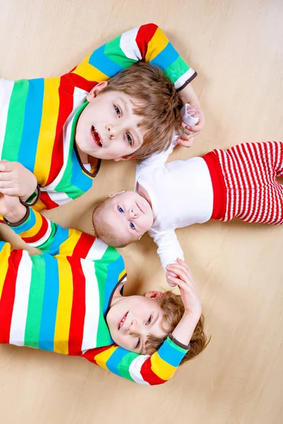 Two happy little preschool kids boys with newborn baby girl, cute sister. Siblings, twins children and baby playing together. Kids bonding. Family of three, love. kids in colorful fashion clothes. — Stock Photo, Image