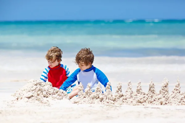 Due ragazzini si divertono con la costruzione di un castello di sabbia sulla spiaggia tropicale delle Maldive. bambini che giocano insieme durante le loro vacanze Gemelli, Fratelli felici che ridono e sorridono . — Foto Stock