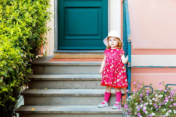 Ritratto di bella piccola gorgeus bella bambina in abiti look estivi rosa, abito alla moda, calzini al ginocchio e cappello. Felice bambino sano in posa davanti a casa colorata. — Foto Stock