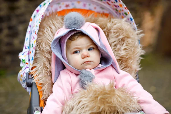 Söt liten vacker liten flicka sitter i barnvagn eller barnvagn på höstdagen. Glad leende barn i varma kläder, mode elegant rosa baby rock med kanin öron. Barnet går på en promenad med föräldrar. — Stockfoto