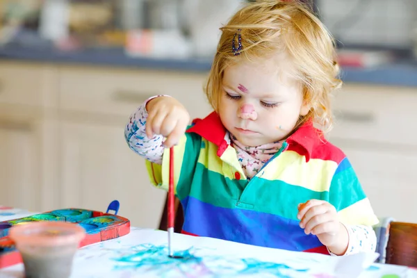 Bonito adorável bebê menina aprendendo pintura com cores de água. Criança pequena desenhando em casa, usando pincéis coloridos. Filha feliz saudável experimentando com cores, água em casa ou no berçário. — Fotografia de Stock