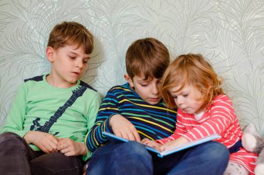 İki okul çocuğu ve küçük kız birlikte kitap okuyorlar. Ağabeyi kitabı tutuyor ve kardeşi için yüksek sesle okuyordu. Aile birlikte vakit geçiriyor. Üç çocuk..