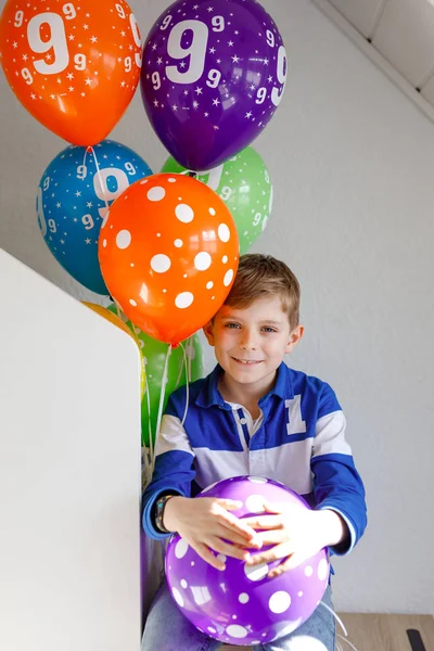 Portrait of happy kid boy with bunch on colorful air balloons on his birthday. Smiling school child having fun, celebrating nineth birth day. Family and best friend party