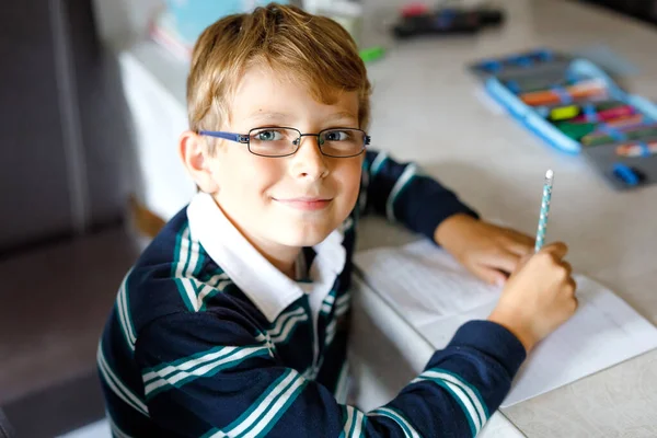 Menino pensativo com óculos em casa fazendo trabalhos de casa, escrevendo texto com canetas coloridas. Criança a fazer exercício, dentro de casa. Ensino fundamental e educação — Fotografia de Stock