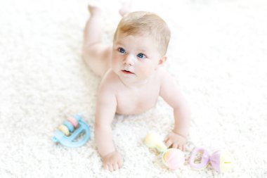 Renkli pastel antika çıngıraklı oyuncakla oynayan şirin bir bebek. Yeni doğmuş bir çocuk, küçük bir kız kameraya bakıyor ve emekliyor. Aile, yeni hayat, çocukluk, başlangıç konsepti. Bebek yakalama