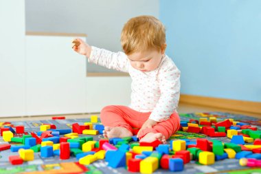 Eğitici oyuncaklarla oynayan sevimli bir kız bebek. Mutlu sağlıklı bir çocuk, evdeki renkli tahta bloklarla eğleniyor. Bebek öğrenme renkleri ve biçimleri