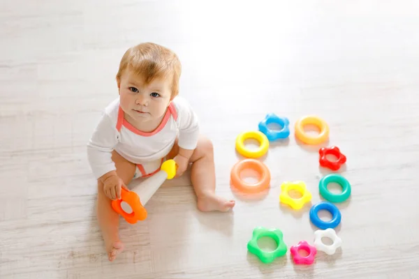 Bebek odasında eğitici oyuncaklarla oynayan güzel bir kız. Mutlu sağlıklı çocuk evde renkli farklı oyuncaklarla eğleniyor. Plastik piramit yapmaya çalışan ve harflerle blok kullanan çocuk. — Stok fotoğraf
