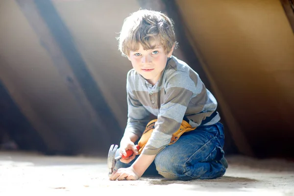 Happy little kid boy helping with toy tools on construction site. Funny child of 6 years having fun on building new family home. Kid with nails and hammer helping father to renovate old house — Stock Photo, Image
