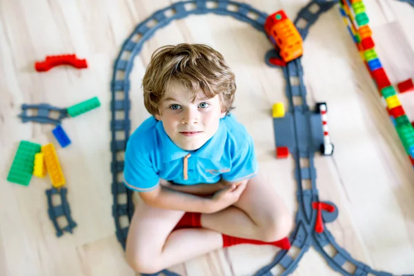 Menino loiro adorável brincando com blocos de plástico coloridos e criando estação de trem. Criança se divertindo com a construção de brinquedos ferroviários em casa — Fotografia de Stock