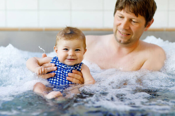 Happy middle-aged father swimming with cute adorable baby daughter in whirl pool. Smiling dad and little child, girl of 6 months having fun together. Active family spending leisure in spa hotel