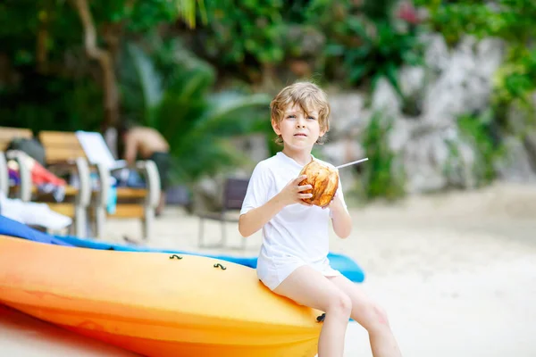 Un niño divertido y encantador bebiendo jugo de coco en la playa del océano. niño jugando en vacaciones familiares en la isla tropical. verano, felicidad, concepto de infancia — Foto de Stock