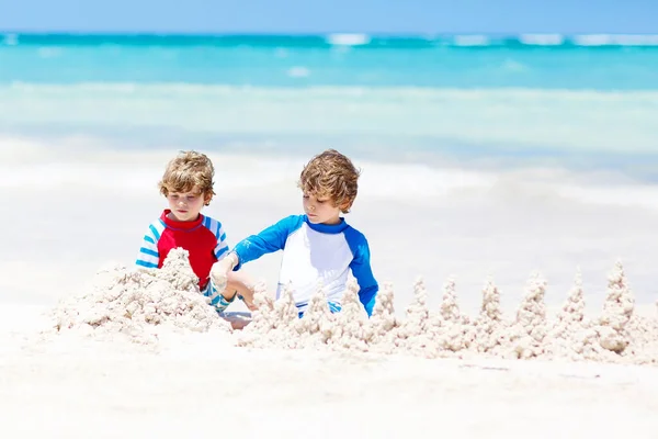 Two little kids boys having fun with building a sand castle on tropical beach of Maldives. children playing together on their vacations — Stock Photo, Image