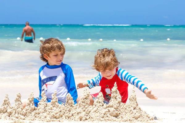 Due ragazzini che si divertono con la costruzione di un castello di sabbia sulla spiaggia tropicale sull'isola. Bambini sani che giocano insieme durante le loro vacanze. Gemelli, fratelli felici che ridono e sorridono — Foto Stock