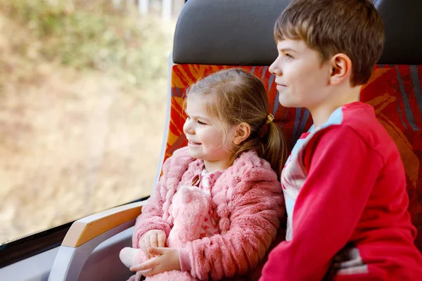 可爱的小女孩和弟弟小男孩坐在火车上，望着窗外。两个可爱的健康快乐的孩子在一起玩乐。正在铁路上享受家庭度假的兄弟姐妹们 — 图库照片