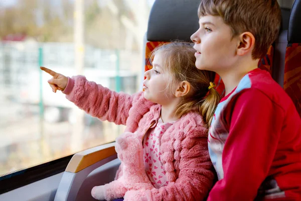 Linda niñita y hermano niño niño sentado en el tren y mirando por la ventana. Dos adorables niños felices y sanos divirtiéndose juntos. Hermanos sonrientes que se van de vacaciones familiares por ferrocarril — Foto de Stock