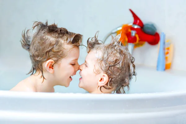 Irmãos felizes: Duas crianças gêmeas saudáveis brincando junto com a água tomando banho na banheira em casa. Os miúdos divertiram-se juntos. crianças lavando cabeças e cabelos com xampu. — Fotografia de Stock
