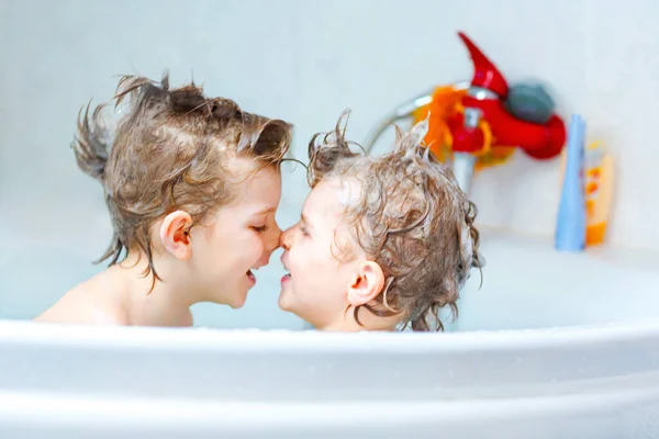 Felices hermanos: Dos pequeños gemelos sanos jugando juntos con agua tomando un baño en la bañera en casa. Chicos divirtiéndose juntos. niños lavando cabezas y pelos con champú. —  Fotos de Stock