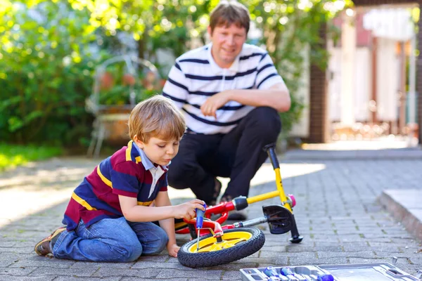 Adorable niño y padre cadena de reparación en bicicletas y cambio de rueda de bicicleta de equilibrio. Familia, padre e hijo trabajan juntos con herramientas de trabajo al aire libre. Ocio activo —  Fotos de Stock