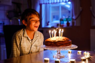 Sevimli, mutlu, küçük sarışın çocuk doğum gününü kutluyor. Çocuk ev yapımı kek üzerine mum üflüyor, kapalı alanda. Okul çocukları için doğum günü partisi, aile kutlaması