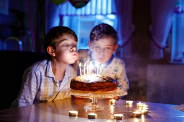İki mutlu sarışın çocuk doğum gününü kutluyor. Çocuklar ev yapımı pastaya mum üflüyorlar. Okul çocukları için doğum günü partisi, ikizler için aile kutlaması.