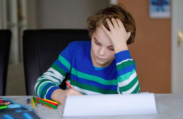 Porträt eines süßen, glücklichen Schuljungen, der zu Hause Hausaufgaben macht. Kleines Kind schreibt mit Buntstiften, drinnen. Grundschule und Bildung. Kind lernt Buchstaben und Zahlen schreiben — Stockfoto