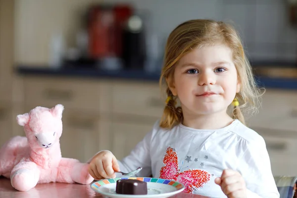 かわいい面白い幼児の女の子は自宅でチョコレートアイスクリームを食べています。幸せな健康な赤ん坊の子供は甘いアイスクリームと豪華なラマのおもちゃを供給する。デザートプリンを楽しむ素敵な子供. — ストック写真