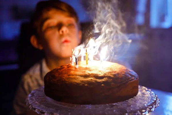 Schattige blonde kleine jongen die zijn verjaardag viert. Kind blaast kaarsen op zelfgebakken taart, binnen. Verjaardagsfeest voor schoolkinderen, familiefeest — Stockfoto