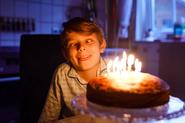 Schattige blonde kleine jongen die zijn verjaardag viert. Kind blaast kaarsen op zelfgebakken taart, binnen. Verjaardagsfeest voor schoolkinderen, familiefeest — Stockfoto