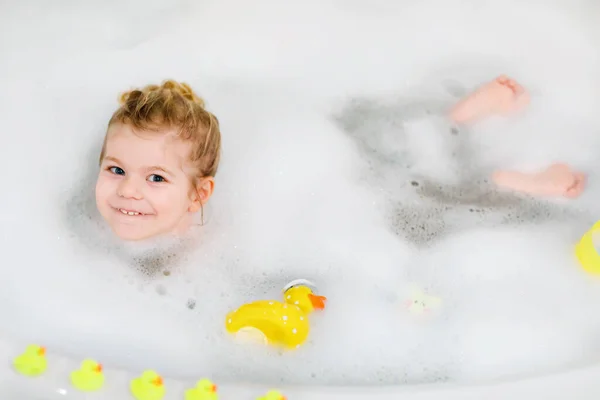 Söt söt liten flicka som badar i badkaret. Glad frisk baby barn leka med gula gummi tuggummi leksaker och ha kul. Tvätt, städning, hygien för barn. — Stockfoto