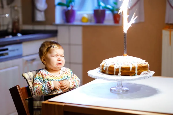 Roztomilá plačící holčička slaví první narozeniny. Dítě se bojí ohňostroje na pečeném dortu, uvnitř. Batole není šťastné. — Stock fotografie