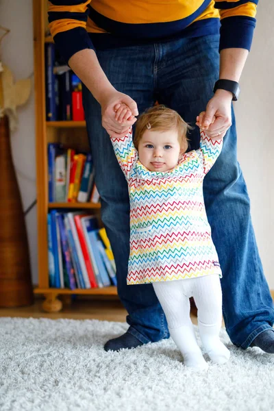 Adorable baby girl of twelve months or one year making first steps. Father teaching daughter walking. Holding by hands. Family in love — Stock Photo, Image