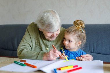 Güzel bir kız ve büyükanne evde keçeli kalemle resim çiziyorlar. Tatlı çocuk ve son sınıf öğrencisi birlikte eğleniyorlar. Mutlu aile içeride.