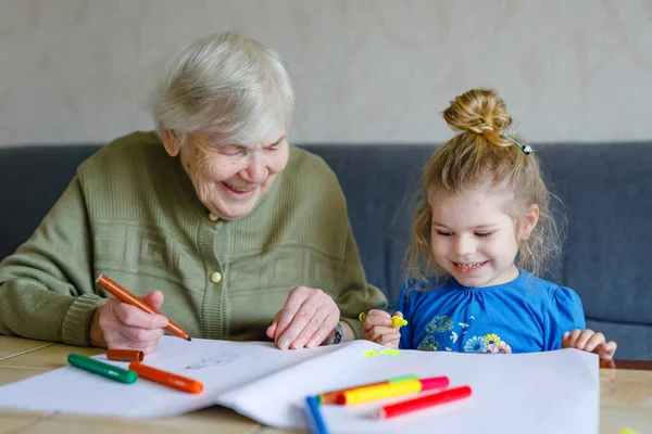 Prachtig peuter meisje en overgrootmoeder tekenen samen foto 's met vilten pennen thuis. Schattig kind en oudere vrouw die samen plezier hebben. Gelukkig gezin binnen — Stockfoto