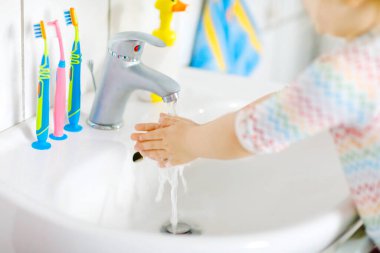 Küçük bir kızın banyoda ellerini sabunla ve suyla yıkaması. Çocuğun vücut parçalarını temizlemeyi öğrenmesini kapat. Virüs salgını sırasında yapılan hijyen rutini. Çocuk evde ya da çocuk odasında..